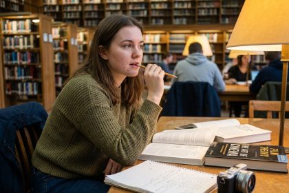 Étudiante en cinéma révisant ses cours dans une bibliothèque universitaire entourée de manuels de réalisation et d'une caméra